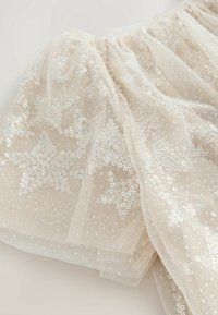 Tissu en tulle couleur crème avec taille froncée, orné de motifs d’étoiles en sequins blancs pour un effet scintillant.