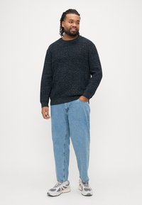 Tamsiai mėlynas tekstūruotas mezgimo megztinis su apvaliu kaklu, derinamas su šviesiai mėlynais laisvais džinsais ir pilkais sportiniais bateliais. Minimalūs aksesuarai.