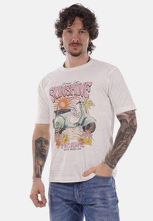 Uomo con capelli ricci e tatuaggi che indossa una maglietta bianca con una grafica di uno scooter vintage, sole, fiori e la scritta "SUNSHINE PARADISE".