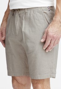 Beige stripete shorts laget av lett materiale. Har strikkedetalj i livet og sidelommer. Akkompagnert med en liten logomerking.