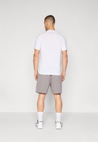 Valge lühikeste varrukatega spordipoliis, mille alla on sobitatud hallid lühikesed püksid. Polaril on ümmargune kaelus ja logo detail seljal. Kingad on mustad ja valged.