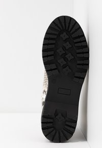 Semelle en caoutchouc noir d'une botte avec un motif de bande de roulement profond, taille marquée 37, photographiée debout sur fond blanc.