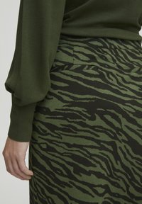 Grön tröja med puffärmar, kombinerad med en figursydd kjol med ett mönster av svart och mörkgrön tigerstrimma samt bakfickor.