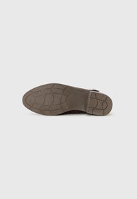Semelle en cuir brun avec une surface en caoutchouc texturé, dotée d'un motif de semelle pour l'adhérence et le soutien. Bout arrondi et léger talon.