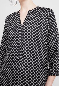 Blusa nera con maniche a tre quarti, caratterizzata da un motivo floreale bianco. Design a V e tessuto morbido con una vestibilità rilassata.