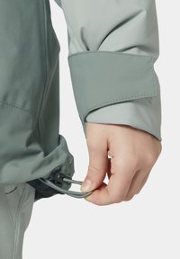 Lehká bunda v šedozelené tkanině s manžetou na suchý zip a staženým lemem, který upravuje ruka.