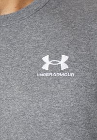 Grau Baumwoll-T-Shirt mit rundem Ausschnitt, mit einem weißen gestickten Under Armour-Logo auf der linken Brustseite. Glatte Textur.