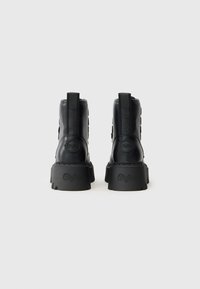 Botas de plataforma de cuero negro con suelas gruesas y tiradores, marcadas con "Buffalo" en el tacón y la suela, mostradas desde la parte de atrás sobre un fondo blanco.