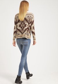 Brun och krämfärgad mönstrad trapper med geometriska mönster, ihop med blå skinny jeans och svarta ankelstövlar.