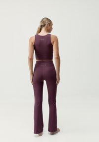 Conjunto de ropa deportiva en color burdeos que incluye una camiseta corta y leggings acampanados. Tejido suave y elástico con un detalle de logo minimalista en la parte posterior.