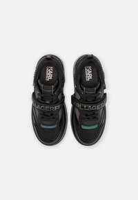 Sneakers i svart syntetmaterial med reflekterande detaljer, featuring en bred rem med "KARL LAGERFELD"-logotyp och texturerad detaljer.