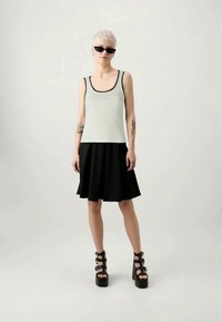 Camisola cinza sem mangas com acabamento preto, combinada com uma saia preta evasê. Apresenta sapatos pretos de plataforma com tiras e cabelo curto e claro.