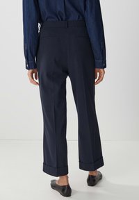 Marinblå skräddarsydda byxor med rak bendesign, med uppvikta muddar och bakfickor. Matchas med en denimskjorta och platta skor.