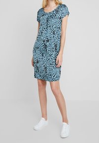 Niebieska sukienka w zwierzęcy wzór z krótkimi rękawami, okrągłym dekoltem i luźnym krojem. Połączona z białymi trampkami dla casualowego wyglądu.