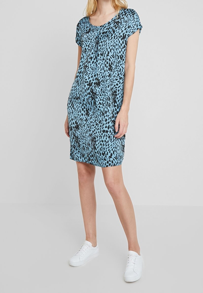 Niebieska sukienka w zwierzęcy wzór z krótkimi rękawami, okrągłym dekoltem i luźnym krojem. Połączona z białymi trampkami dla casualowego wyglądu.