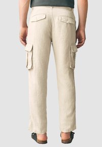 Pantalones cargo de color beige con un corte holgado, fabricados en un tejido ligero. Cuentan con dos bolsillos laterales y dos bolsillos traseros con cierres de botón.