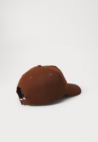 Cappello di cotone marrone con visiera curva, cinturino regolabile sul retro e dettagli di cucitura visibili. Design semplice e sobrio.