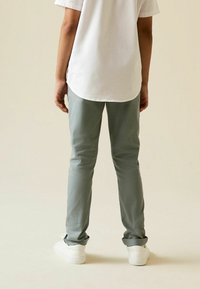 Pantaloni grigio chiaro, slim-fit, con risvolti, realizzati in cotone, abbinati a una camicia bianca a maniche corte e sneakers bianche.