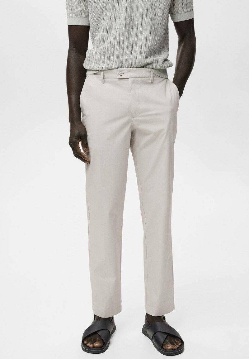 Pantalon beige clair en tissu lisse, avec une taille plate, des passants de ceinture et des poches latérales, associé à des sandales noires à enfiler.