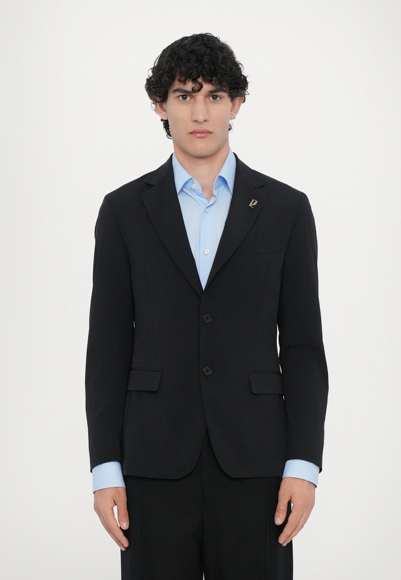 Schwarzer Blazer mit figurbetontem Design, zwei Knöpfen und Vorderaschen. Darunter ein hellblaues Hemd mit Button-down-Kragen und aufgerollten Manschetten.
