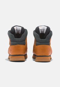 Botas de tobillo de cuero marrón con forro de tela gris, punta redonda y suela de goma. Presentan un logotipo en el talón exterior y etiquetas visibles en el interior.