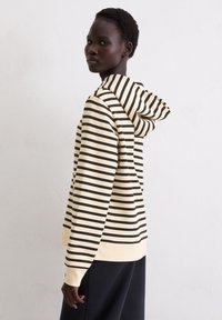 Gestreepte hoodie in crème en zwart, met een relaxte pasvorm, lange mouwen en een capuchon. Zacht materiaal met geribbelde manchetten en zoom.
