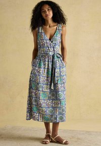 Maxikleid aus gemustertem Stoff mit floralen und geometrischen Motiven in Blau, Grün und Gelb. Mit einem Bindeband in der Taille und Taschen.