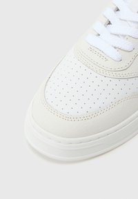 Bijela kožna tenisica s perforiranim prednjim dijelom, podstavljenim ovratnikom i ravnim bijelim vezicama. Debeli gumeni potplat s diskretnim detaljima šavova.