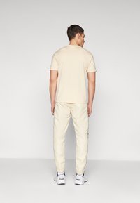 Bēša īsām piedurknēm t-krekls ar apaļu kakla izgriezumu, saskaņots ar atbilstošām bēšām sporta biksēm ar šauru piegriezumu un elastīgām aprocēm. Baltas sporta kurpes.