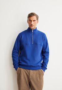 Blauwe fleece pullover met een hoge hals en een rits aan de voorkant, met een textuurafwerking en een ingenaaid logo op de borst.