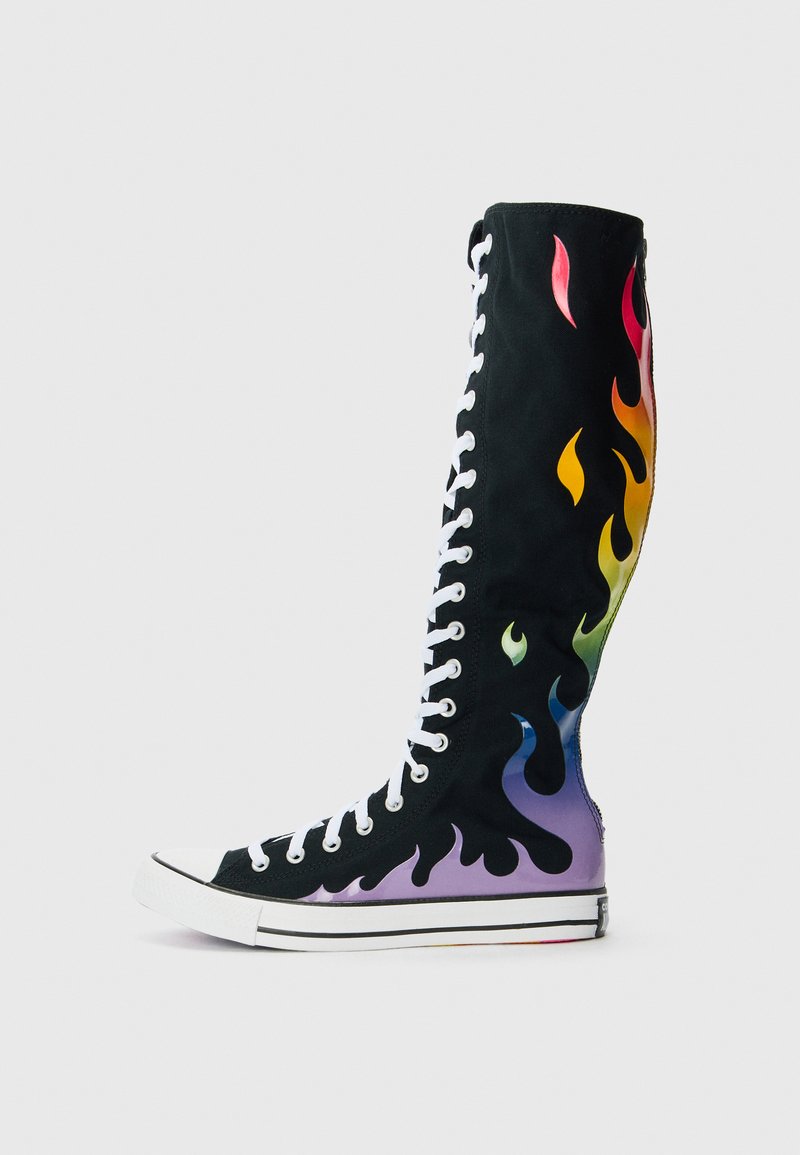 High-top boot made of black canvas featuring multicolored flame patterns, white laces, and a contrasting purple sole with a striped edge.