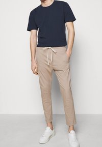 Navy crew-neck t-shirt, beige drawstring pants, and white sneakers. Pants feature a relaxed fit and side pockets. Smooth fabric, minimal design.