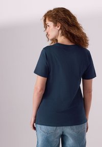 Temno modra bombažna majica s kratkimi rokavi, okroglim ovratnikom in sproščeno prileganjem, kombinirana s svetlo modrimi kavbojkami iz jeansa.