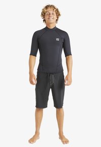 Czarny rash guard z krótkim rękawem z jasnoszarymi przeszyciami i logo, zestawiony z ciemnymi szortami plażowymi z regulowanym sznurkiem.