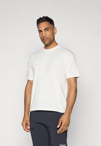 White cotton t-shirt with short sleeves and a classic crew neck, shown with dark shorts, against a plain gray background.
