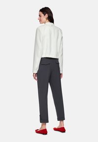 Weiße, kurz geschnittene Jacke mit elastischem Bund, kombiniert mit grauen Hosen mit Klappentaschen und umgeschlagenen Bündchen. Helle rote Ballerinas vervollständigen das Outfit.