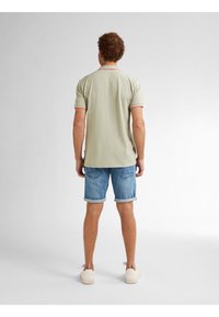 Lichtgroen polo shirt met rode accenten, gecombineerd met opgerolde denim korte broek en witte sneakers. Glad materiaal en casual ontwerp.