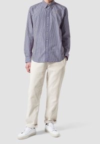 Camicia a righe blu e bianca, con maniche lunghe e un piccolo logo. Indossata con pantaloni di corduroy color crema e sneakers bianche.