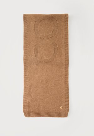 Écharpe en tricot marron pliée avec des motifs circulaires en relief et un petit emblème rond doré près du bord sur un fond blanc.