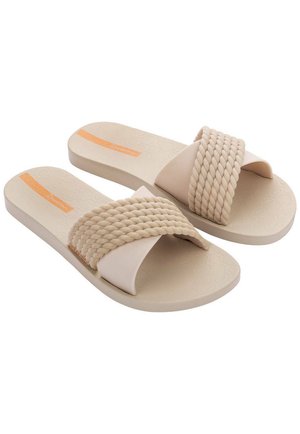 Sandalias de color beige claro con una correa trenzada y suela lisa. Presentan una plantilla texturizada y un sutil acento naranja cerca de la zona de los dedos.