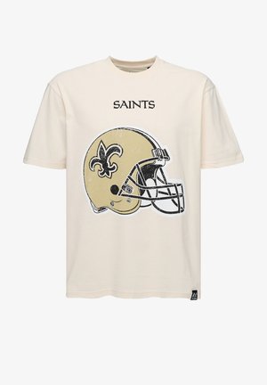 Kremowa koszulka z grafiką w stylu vintage przedstawiającą złotą i czarną hełm sportowy z motywem fleur-de-lis, z napisem "SAINTS" nad wzorem.