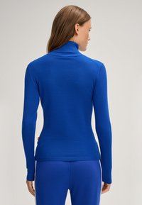 Blauer Rollkragenpullover mit langen Ärmeln, geripptem Hals und Saum, taillierter Schnitt mit glatter Textur. Seitliches Etikett sichtbar.