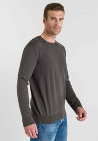 Mörkgrå stickad tröja med rund nacke, ribbade ärmslut och detalj på axlarna, tillsammans med blåjeans. Slät yta och passande design.