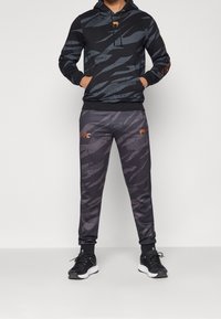 Zwarte hoodie met een grijs abstract patroon, gecombineerd met donkere grijze joggers met vergelijkbare patronen en oranje UFC-logo accenten.