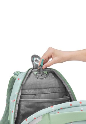 Main ajustant la hauteur d'une sangle de poitrine interne d'un sac à dos vert et à motifs.