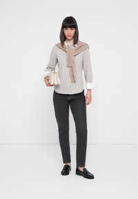 Koszula w paski, beżowy sweter zarzucony na ramiona, ciemne dżinsy, czarne mokasyny, trzymając małą białą torebkę.