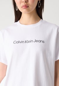 Balta medvilninė marškinėliai su ryškiu juodu „Calvin Klein Jeans“ logotipu. Minkšta tekstūra ir klasikinis apvalus iškirpimas.