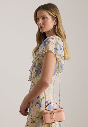 Γυναίκα με μακριά ξανθά μαλλιά που φοράει φόρεμα με floral βολάν και κρατά μια μικρή ρόζ τσάντα χιαστί με χρυσή αλυσίδα.