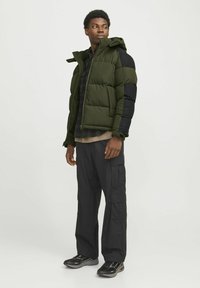 Pufjakke i olivengrøn og sort, med hætte, lynlås foran, kviltet design og en afslappet pasform. Kombineret med sorte cargo-bukser og sneakers.