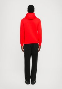 Sudadera roja con capucha de textura suave, combinada con pantalones de pierna ancha negros. Costuras visibles y puños acanalados en la sudadera.